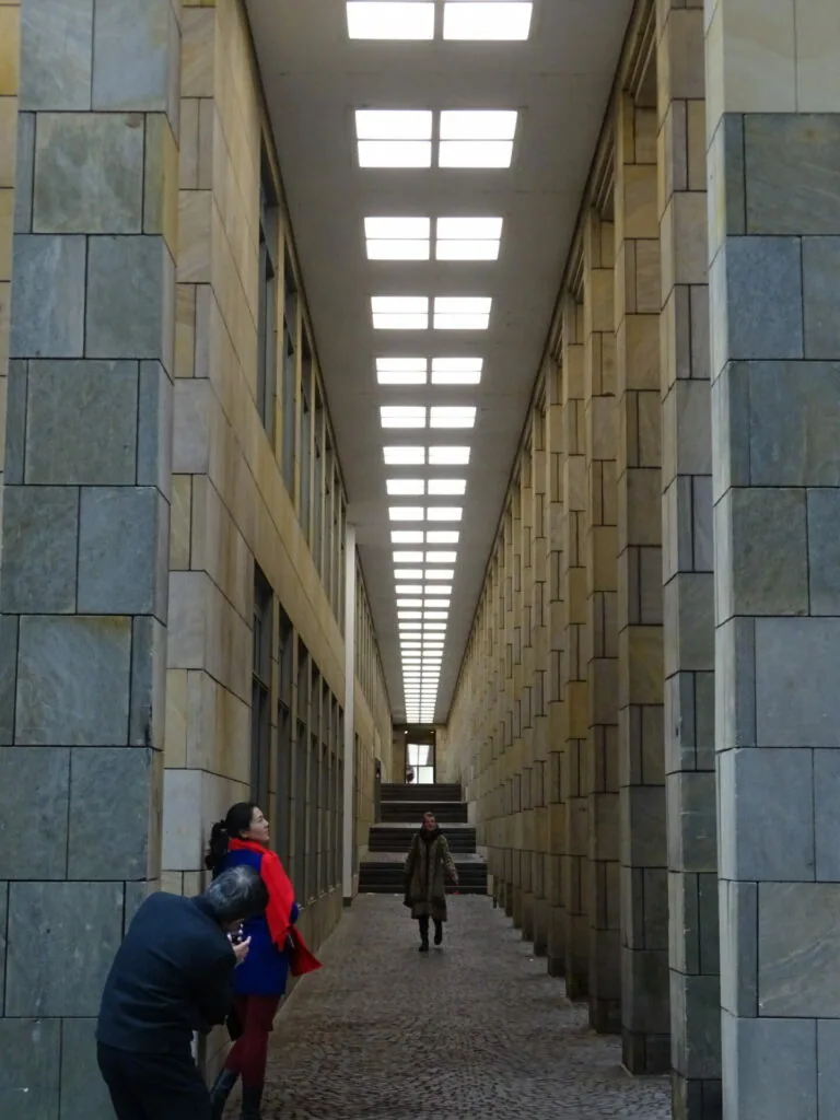 Long narrow corridor with stone tile walls and skylight panels, people walking in distance