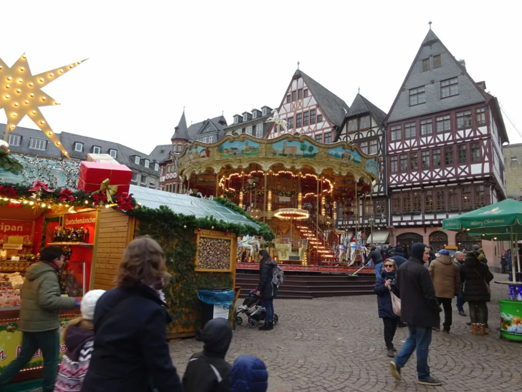 Christmas market in historic town square with carousel, wooden vendor stalls, decorated buildings with half-timbered facades, and golden star decoration