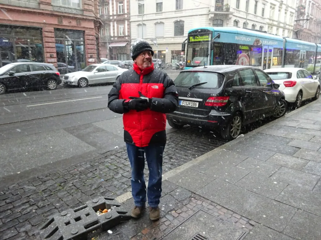 Person in red and black jacket jogging on snowy cobblestone street with parked cars and tram in background