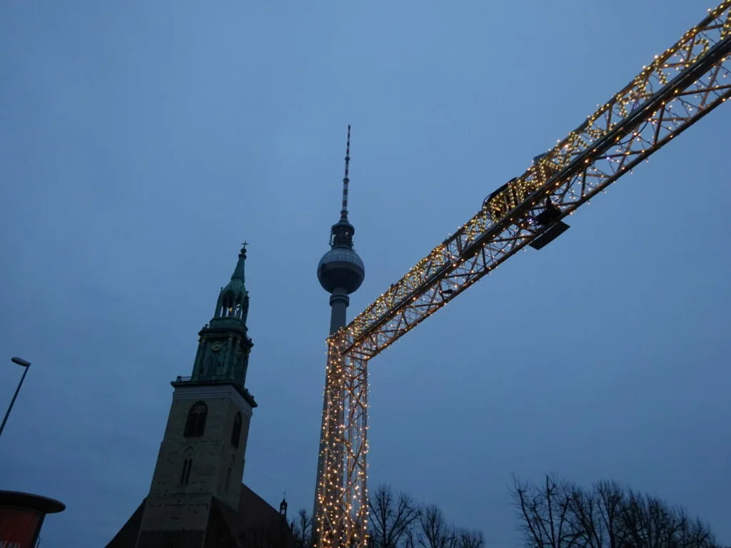 Illuminated archway structure with church spire and broadcast tower at dusk