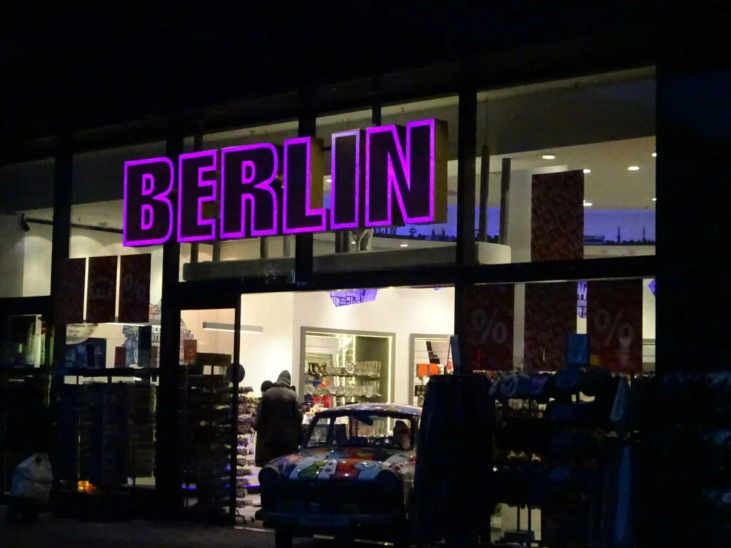 Storefront with bright magenta neon BERLIN sign above illuminated windows displaying clothing and merchandise at night