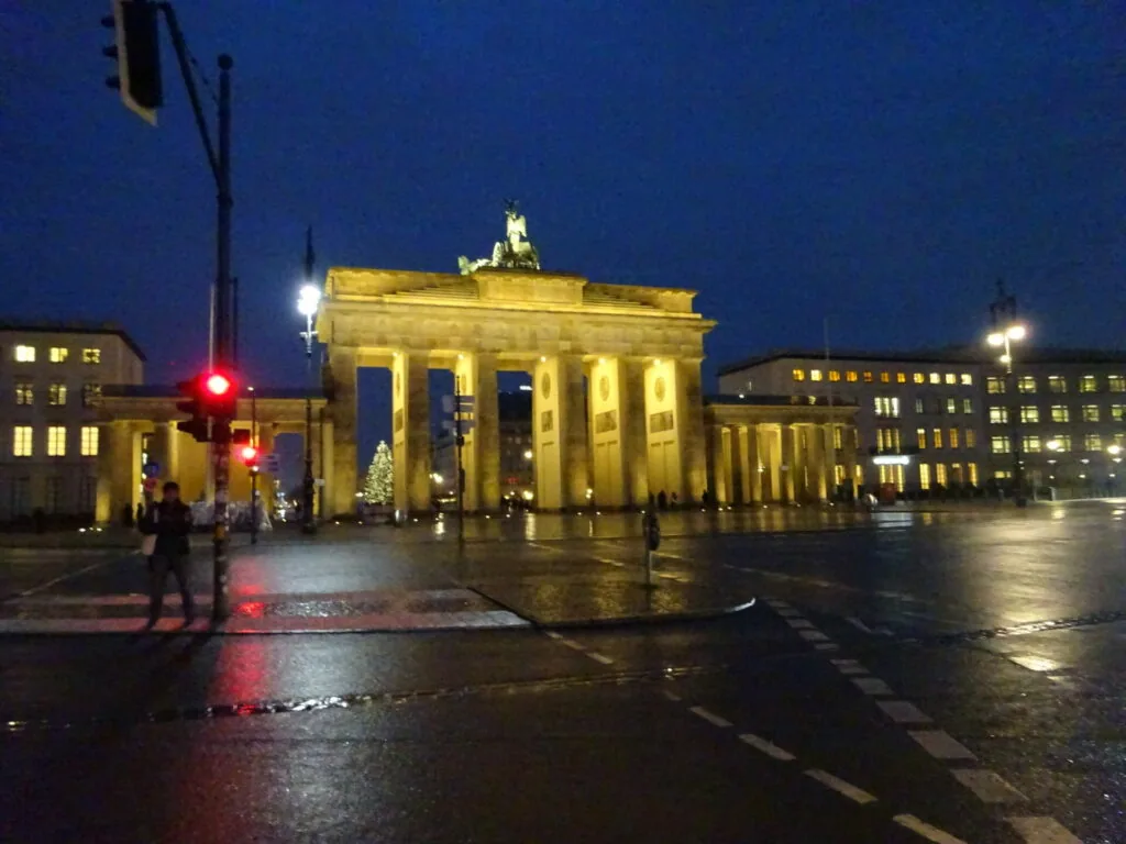 Illuminated neoclassical gate with tall columns at night in wet plaza, historic Berlin landmark